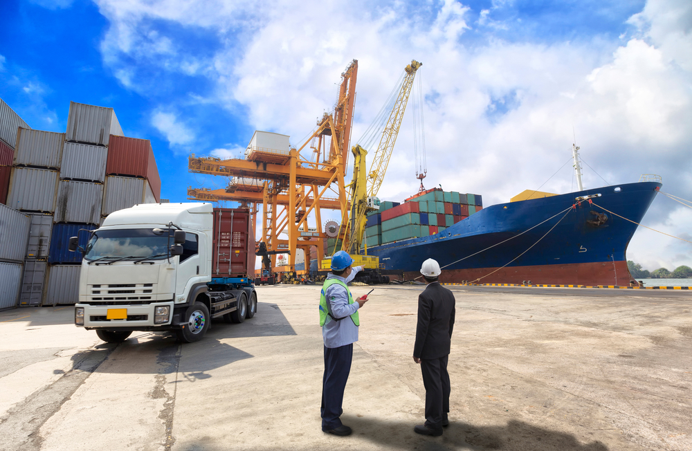 Two people standing in front of a truck and large boat